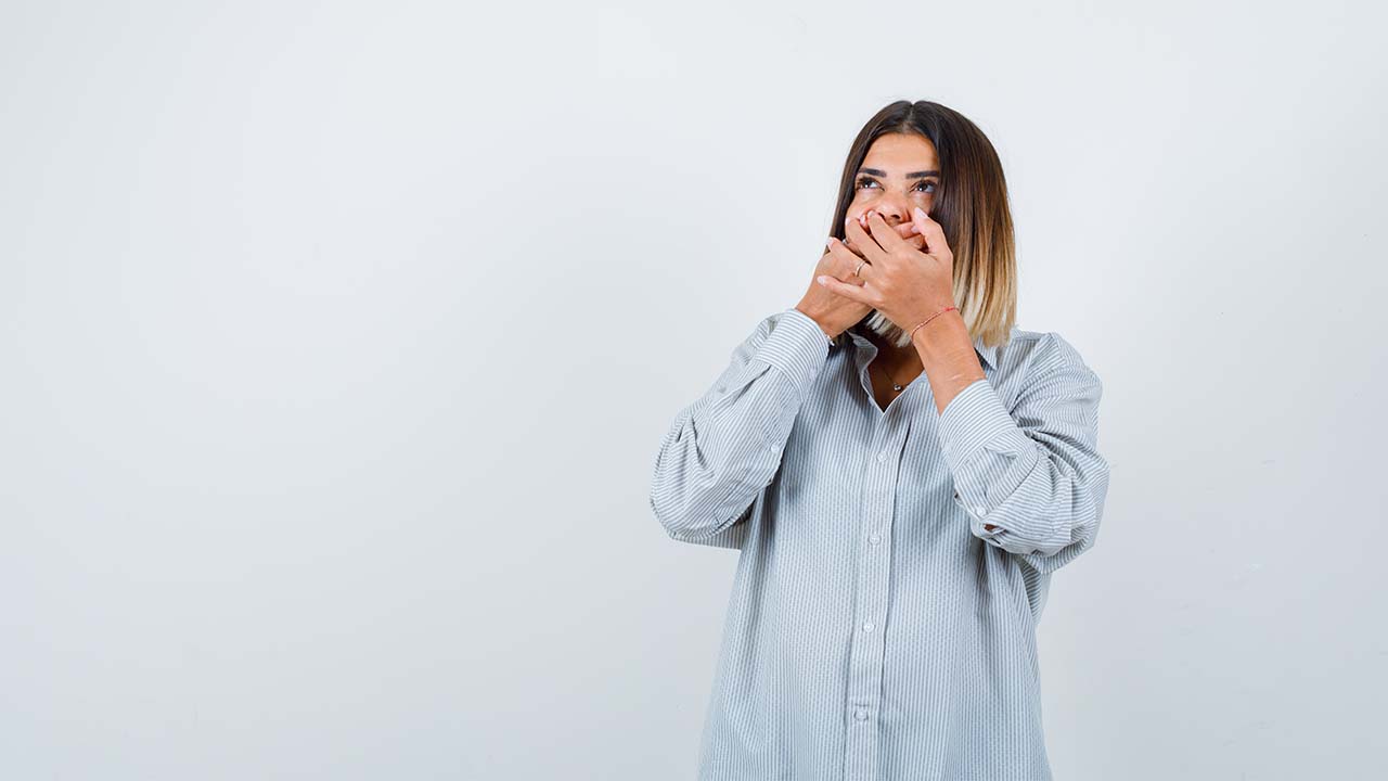 A young woman covering her mouth in pain. She is in need of a periodontist