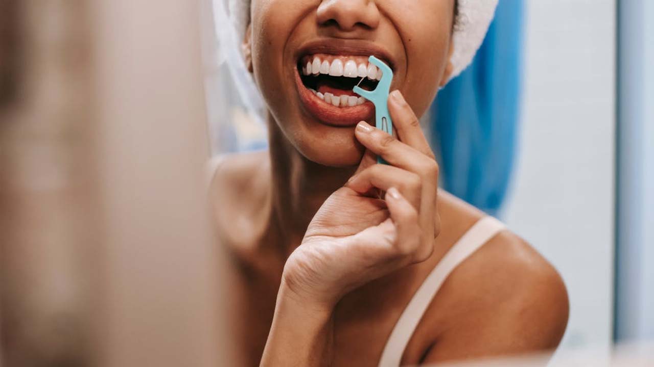 A woman in the bathroom cleaning between her teeth