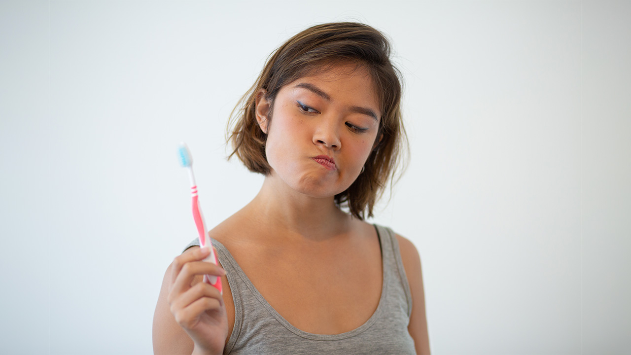 A young woman caught red-handed while studying. She is holding a toothbrush and many questions.