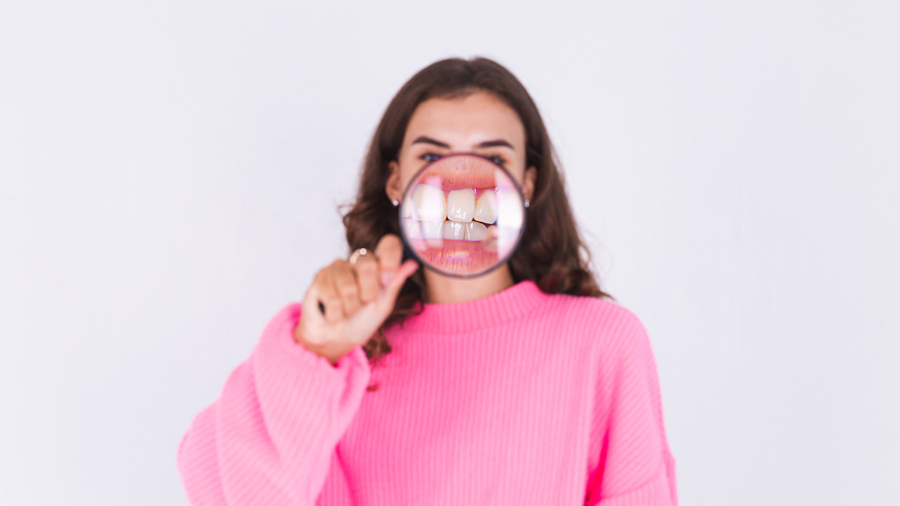 Lady with magnifying glass shows off her clean teeth